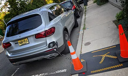 Electric car charging on sidewalk with yellow cones